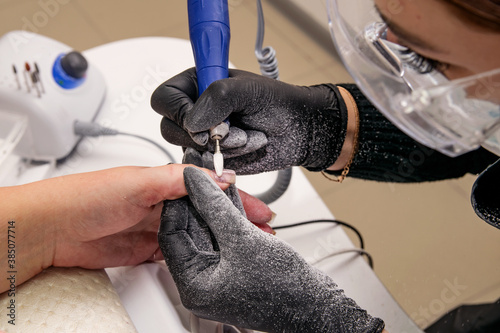 Close-up shot of a master in black gloves removing the coating of gel polish with an apparatus