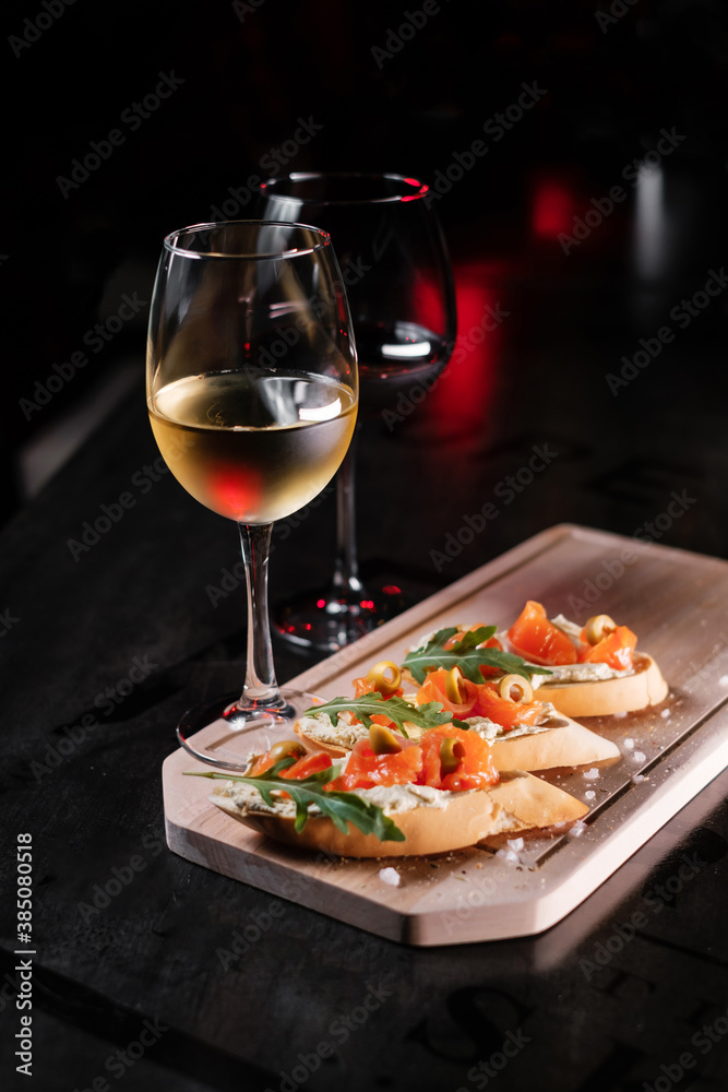 Set of snacks and glasses of wine. Bruschetta with cheese and salmon on a wooden board, served with red wine.