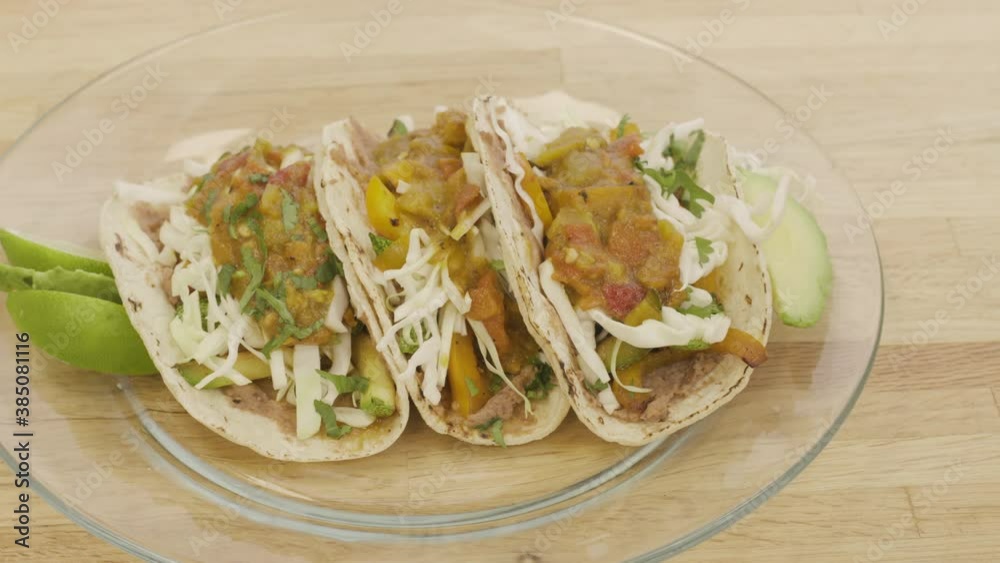 Panning over a plate of tacos. Three vegetarian tacos made with calabacitas and smothered in fresh salsa sit on a butcher block countertop. The fresh and healthy meal is a staple of Mexican cuisine.