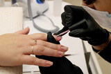 Close-up shot of nail polish by manicurist in black gloves