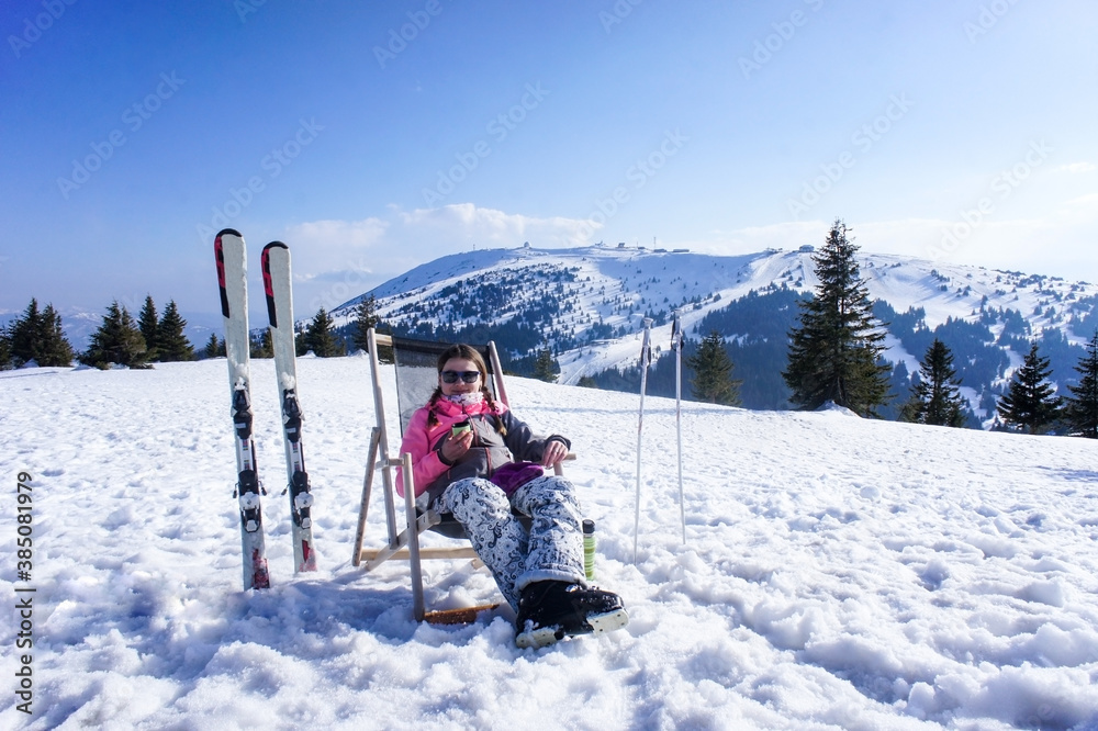 Young woman resting and drinking tea from a thermos after skiing on the ski slope. Winter sports, active lifestyle
