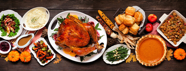 Traditional Thanksgiving turkey dinner. Top view table scene on a dark wood banner background. Turkey, mashed potatoes, dressing, pumpkin pie and sides.