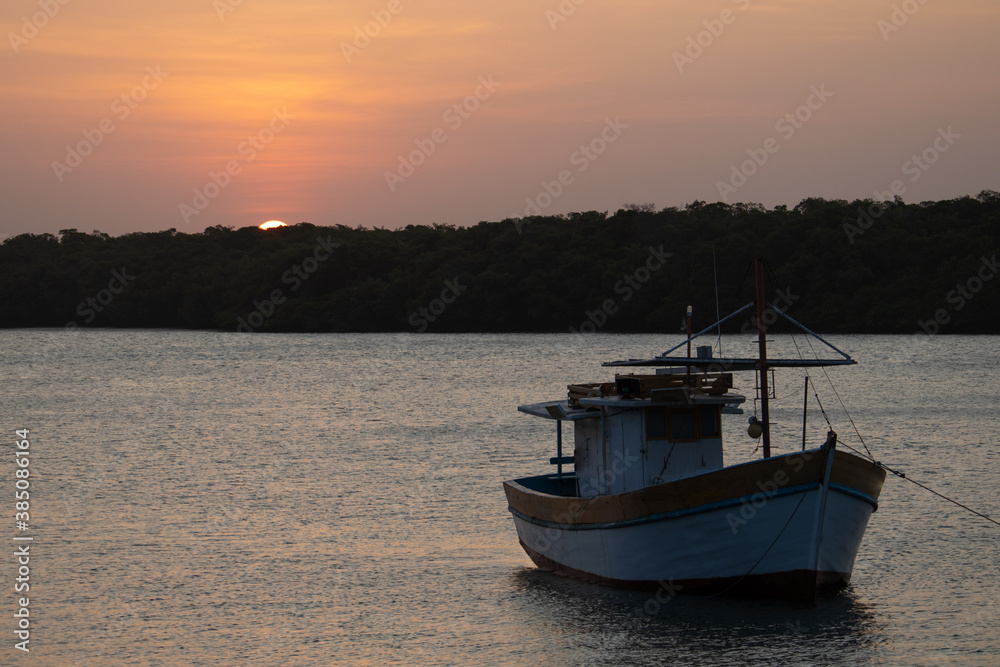 Naklejka premium Sunset over a river with silhouette of a boat
