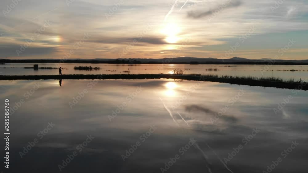 Aerial view fowards, Beautiful sunset over the rice field covered with water. Father and daughter standing on the path. Perfectly smooth surface of water in Albufera National park, Valencia Spain. Aerial view fowards, Beautiful sunset over the rice field covered with water. Father and daughter standing on the path. Perfectly smooth surface of water in Albufera National park, Valencia Spain.