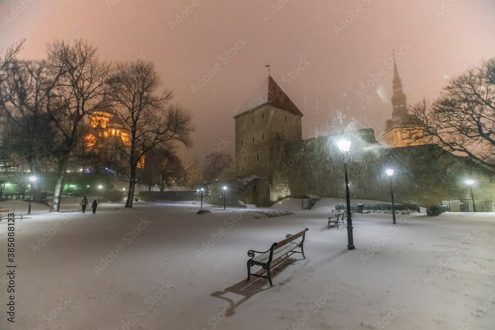Winter night scene with the heavy snowfall of the historic Tallinn town wall,its defensive towers and illuminated churches in the background Winter night scene with the heavy snowfall of the historic Tallinn town wall,its defensive towers and illuminated churches in the background