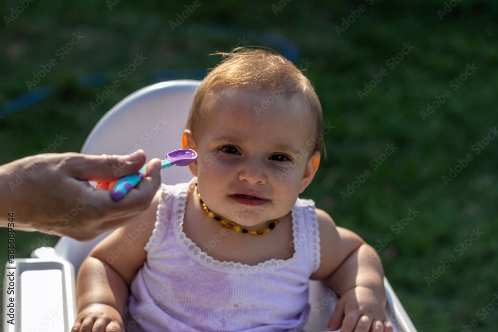 Photo of an unrecognized young mother feeding her baby girl with water outdoors in sunlight. Mothers hand feeding her baby with spoon. Cropped image of mother giving food to her daughter in the nature Photo of an unrecognized young mother feeding her baby girl with water outdoors in sunlight. Mothers hand feeding her baby with spoon. Cropped image of mother giving food to her daughter in the nature