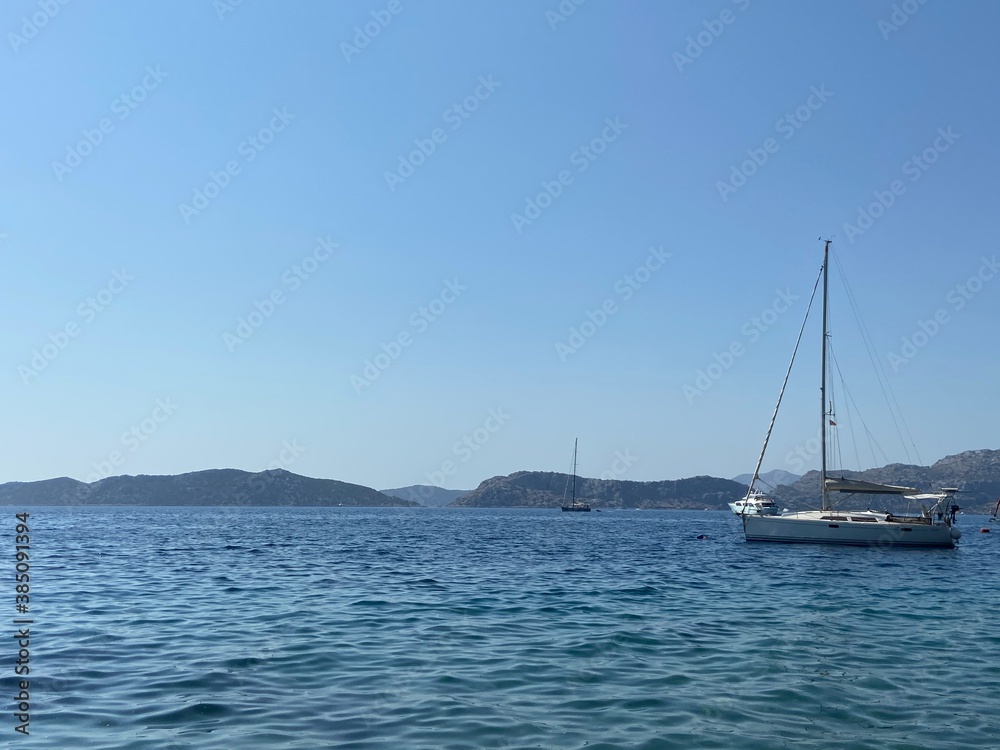 Sailing on blue turquoise waters of Aegean Sea. White yacht in the bay and islands at the horizon. Clear blue skies. 