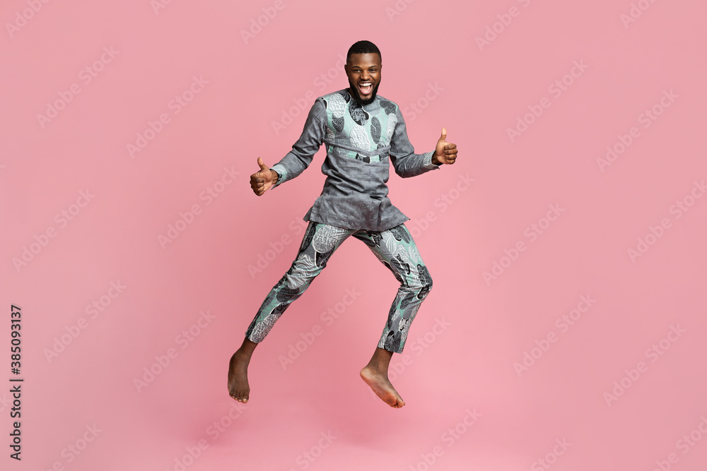 Joyful black guy showing thumbs up and jumping on pink