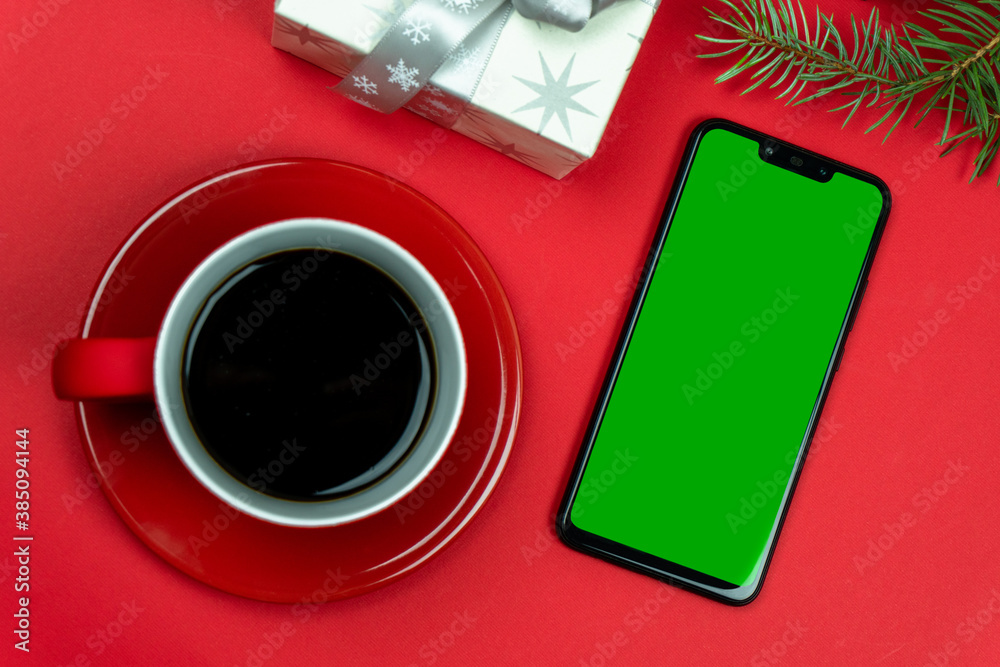 A mobile phone with a place for an inscription or drawing, with a red cup of coffee and gifts for the holiday and a pine branch. A mobile phone with a place for an inscription or drawing, with a red cup of coffee and gifts for the holiday and a pine branch.