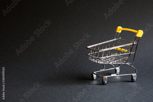 Empty grocery cart from a supermarket on a black background. Black Friday, shopping cart, shopping, online store, sale, discounts. Space for text