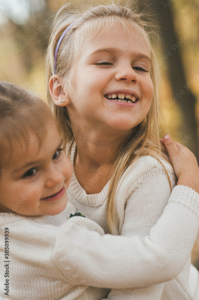 Two cheerful small sisters playing in the park in warm autumn day Two cheerful small sisters playing in the park in warm autumn day