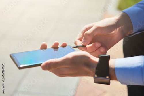 Cropped shot of a businessman using flash drive for smartphone while working outdoors on a sunny day, focus on male hands © Kostiantyn