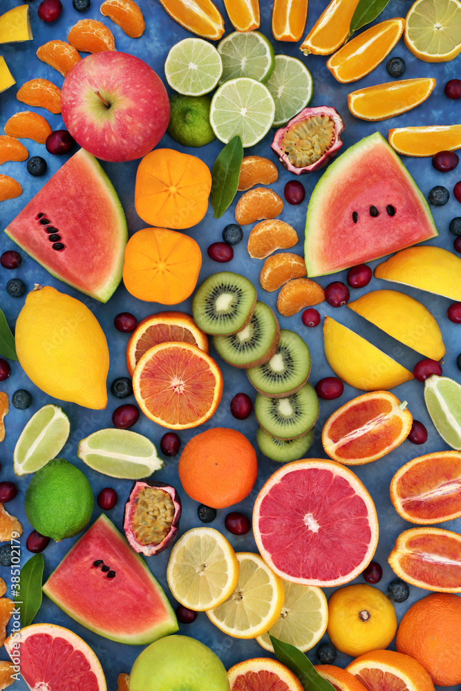 Tropical & citrus fruit for good health forming an abstract background. High in antioxidants, fibre, anthocyanins, lycopene, vitamins & minerals. Immune boosting food. Flat lay on mottled blue.