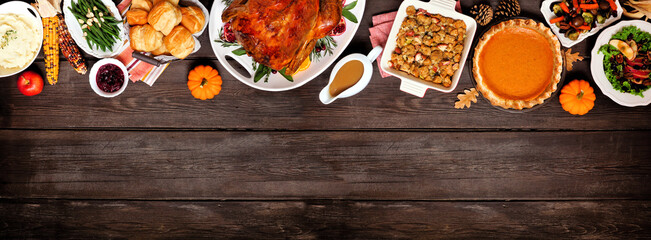 Traditional Thanksgiving turkey dinner. Above view top border on a dark wood banner background with copy space. Turkey, mashed potatoes, dressing, pumpkin pie and sides.