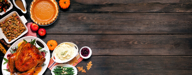 Traditional Thanksgiving turkey dinner. Top down view corner border on a dark wood banner background with copy space. Turkey, mashed potatoes, dressing, pumpkin pie and sides.