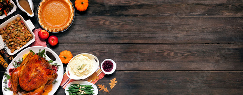 Traditional Thanksgiving turkey dinner. Top down view corner border on a dark wood banner background with copy space. Turkey, mashed potatoes, dressing, pumpkin pie and sides.