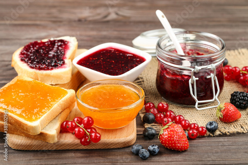 Toasts with jam in bowl and glass jar on wooden table