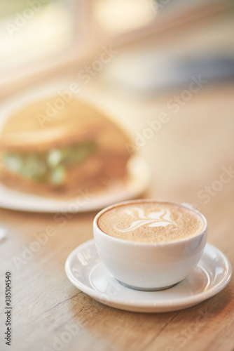 Vertical close up shot of of a cup of coffee cappuccino and sandwich on wooden table in cafe, selective focus