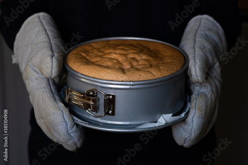 Fotobehang a freshly baked hot cake in a springform pan is held with gloves