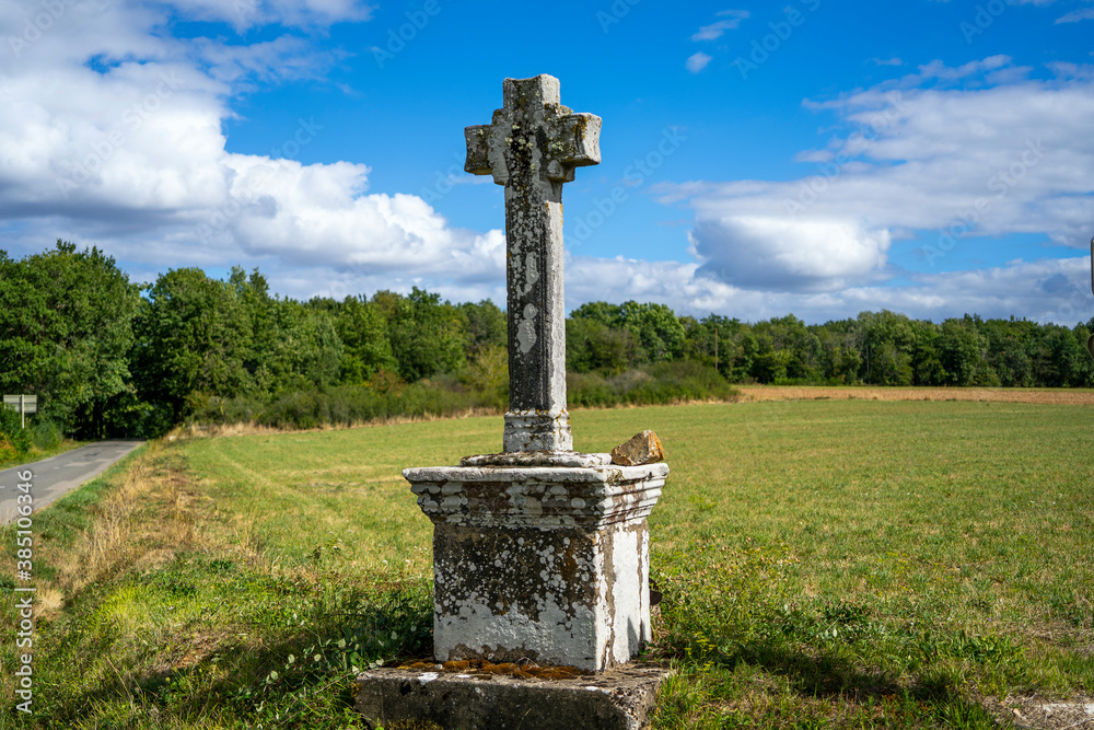 Old stone grey cross standing against background scene of green forest and field at the road crossing Old stone grey cross standing against background scene of green forest and field at the road crossing