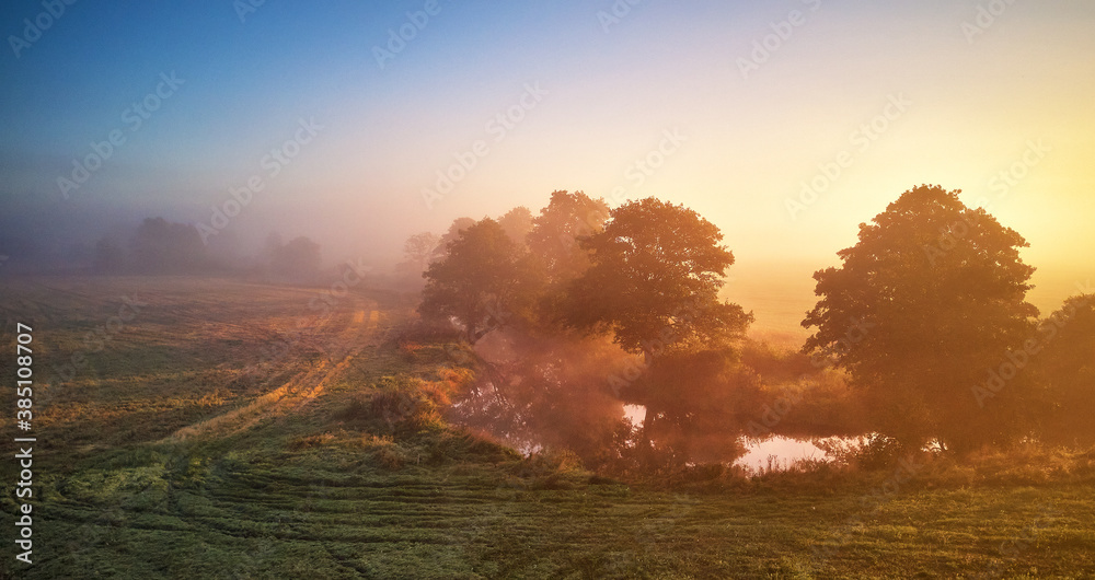 Autumn foggy river sunrise. Colorful misty morning dawn. Fall rural scene panorama