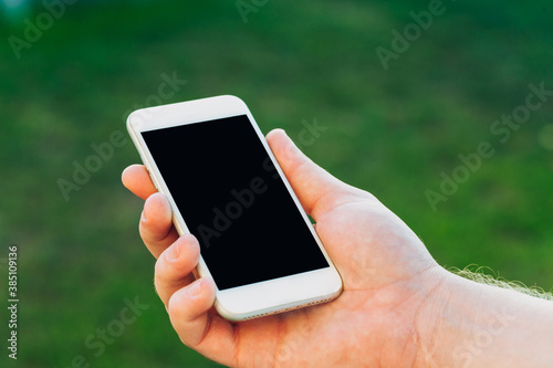 close-up shot of male hands holding smartphone with blank screen copy space for your text message or information content, against green nature background