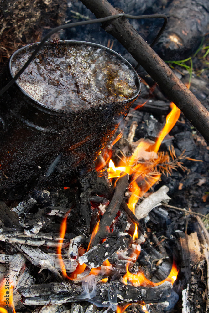 Tourist kettle, kettle in the fire of a burning campfire in a camping trip. Cooking food in the forest on wooden wood during the hike. Active rest and entertainment in nature. Tourist kettle, kettle in the fire of a burning campfire in a camping trip. Cooking food in the forest on wooden wood during the hike. Active rest and entertainment in nature.