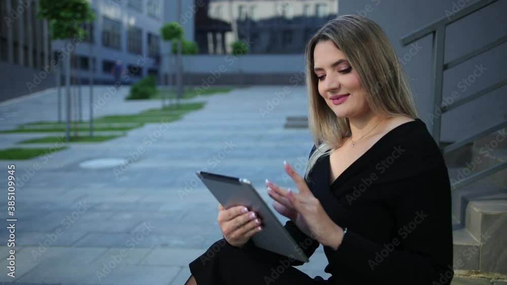 Beautiful young woman using tablet in the city. Business lady holds digital devices pc. Businesswoman and pad. Sitting on a bench outside an office district. Gap between teeth Beautiful young woman using tablet in the city. Business lady holds digital devices pc. Businesswoman and pad. Sitting on a bench outside an office district. Gap between teeth