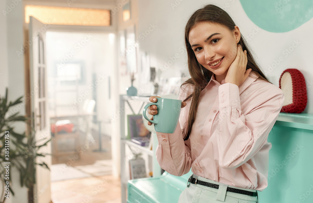 An adorable young longhair brunette looking into a camera smiling holding a cup of tea wearing a designers clothes An adorable young longhair brunette looking into a camera smiling holding a cup of tea wearing a designers clothes