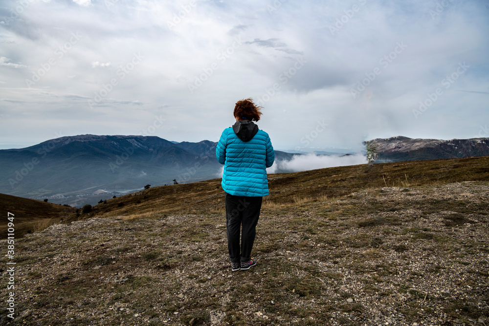 woman tourist in a blue jacket on the top of the mountain at the level of floating clouds