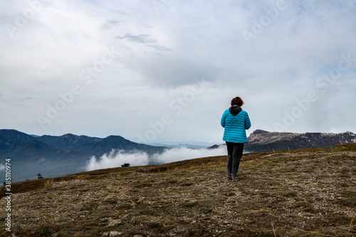 woman tourist in a blue jacket on the top of the mountain at the level of floating clouds © константин константи