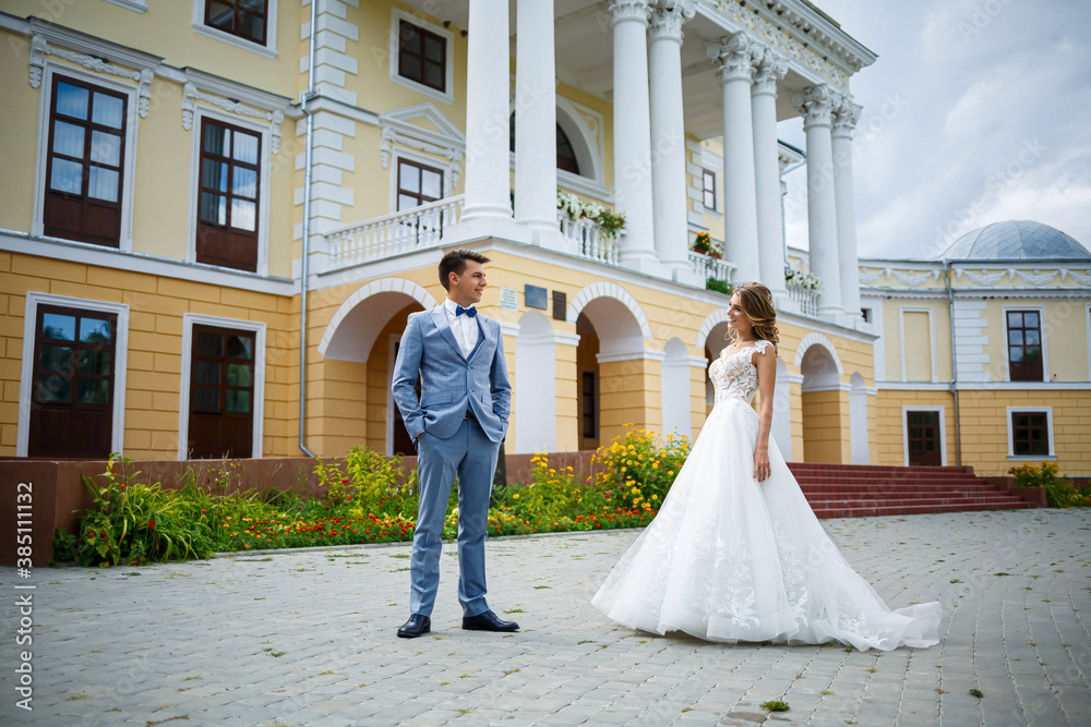 Obraz premium Young stylish guy in a suit the groom and the bride beautiful girl in a white dress with a train walk in the park on their wedding day