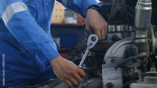 Mechanic Asian man close up fixing repairing car engine automobile vehicle parts examining using tools wrench equipment working hard in workshop garage support and service in overall work uniform