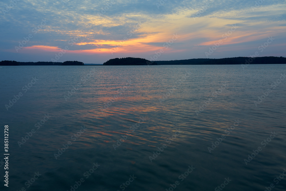 Colorful cloudy sky on a sunset over the sea with horizon on a background and reflection on water.