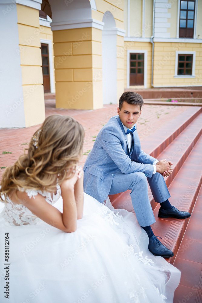 Fototapeta premium Young stylish guy in the costume of the groom and the bride beautiful girl in a white dress with a train walk in the park on their wedding day