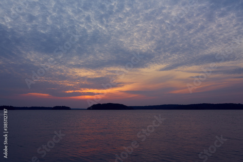 Colorful cloudy sky on a sunset over the sea with horizon on a background and reflection on water. © Arthur
