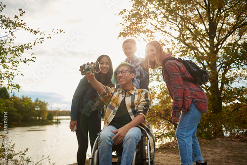 Disabled teen in a wheelchair with multi ethnic group of friends taking a group selfie.