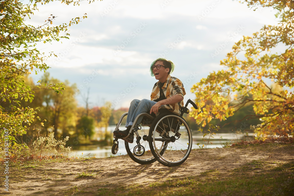 Smiling teenage boy doing wheelie on wheelchair in forest