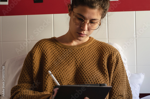 mujer trabajando desde su cama con tablet y computadora