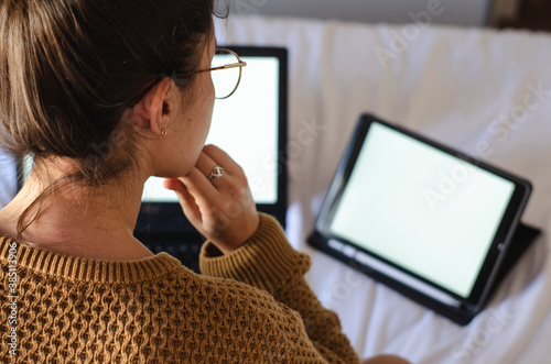 mujer trabajando desde su cama con tablet y computadora
