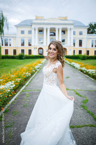 beautiful girl bride in a white dress with a train and a walk turned against the background of a large house with columns on their wedding day