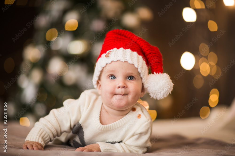 Young baby boy in Christmas cap laying on a bed against Christmas background. Young baby boy in Christmas cap laying on a bed against Christmas background.