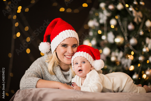 Woman and young baby boy in Christmas cap laying on a bed against Christmas back
