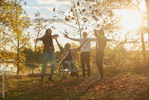 Disabled teen boy playing in Fall leaves with a multi ethnic group of friends.