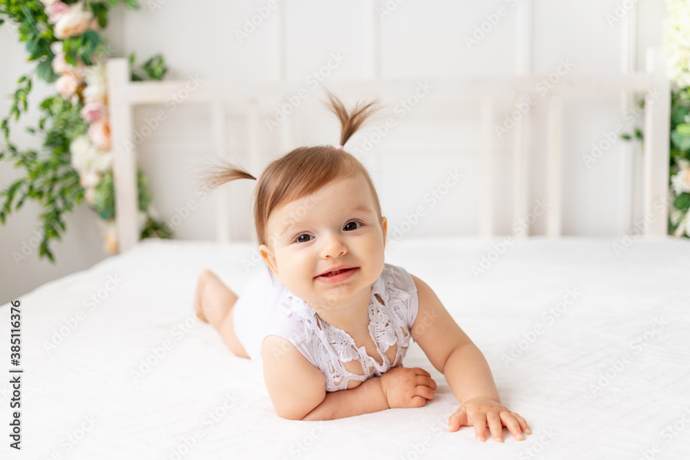 funny baby girl six months old lies in a bright beautiful room on a white bed in a lace bodysuit and smiles funny baby girl six months old lies in a bright beautiful room on a white bed in a lace bodysuit and smiles