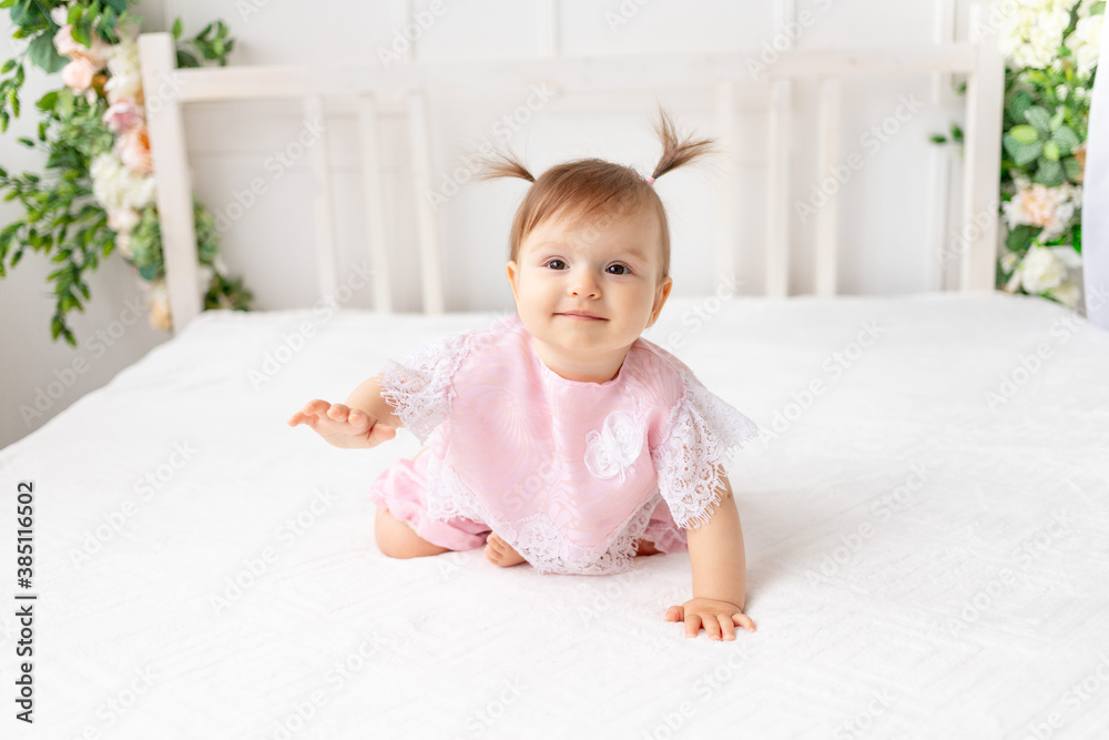 cheerful baby girl six months old sitting in a bright beautiful room on a white bed in pink clothes and smiling cheerful baby girl six months old sitting in a bright beautiful room on a white bed in pink clothes and smiling