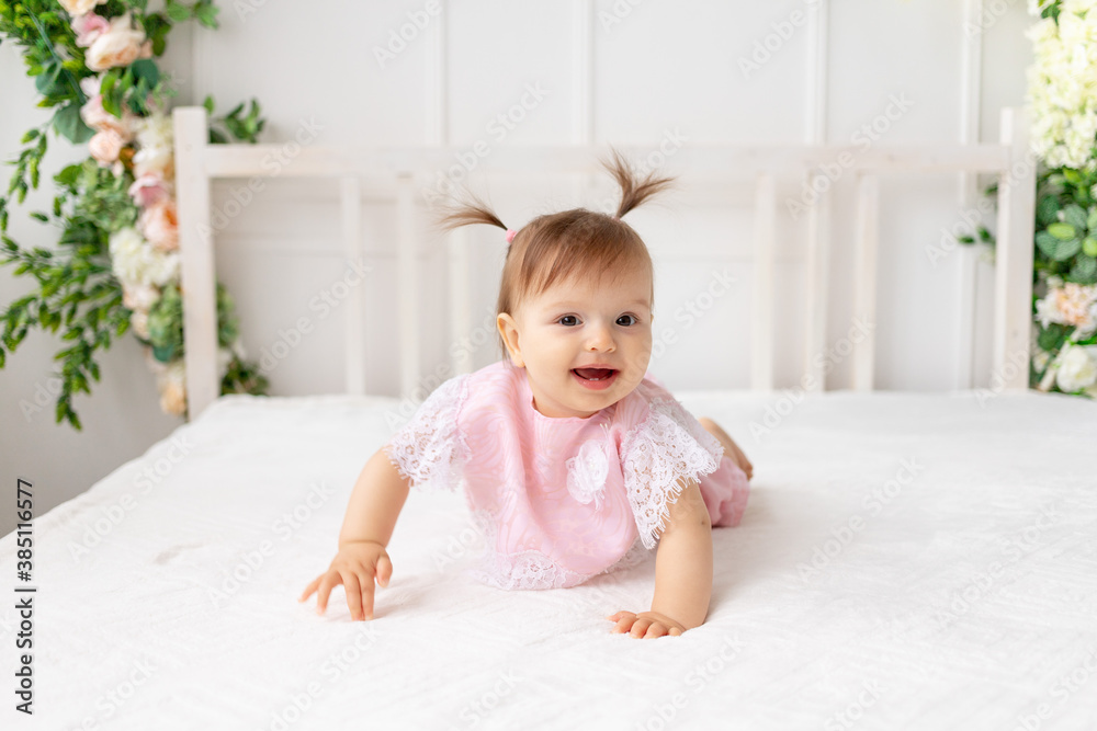 cheerful baby girl six months crawling in a bright beautiful room on a white bed in pink clothes and smiling cheerful baby girl six months crawling in a bright beautiful room on a white bed in pink clothes and smiling
