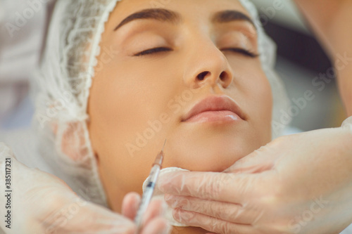 therapists hands in gloves with syringe and cotton pad making botox filler injection in womans underlip