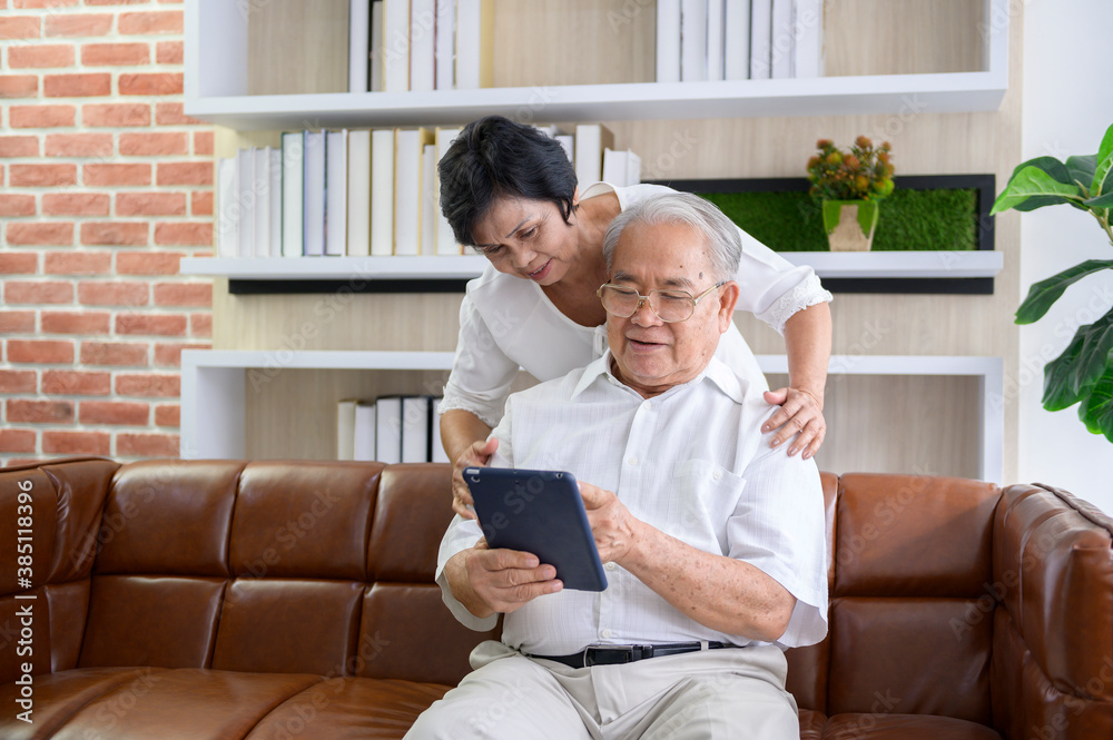 A happy senior Asian couple is using tablet and talking with family on webcam at home, retirement concept.