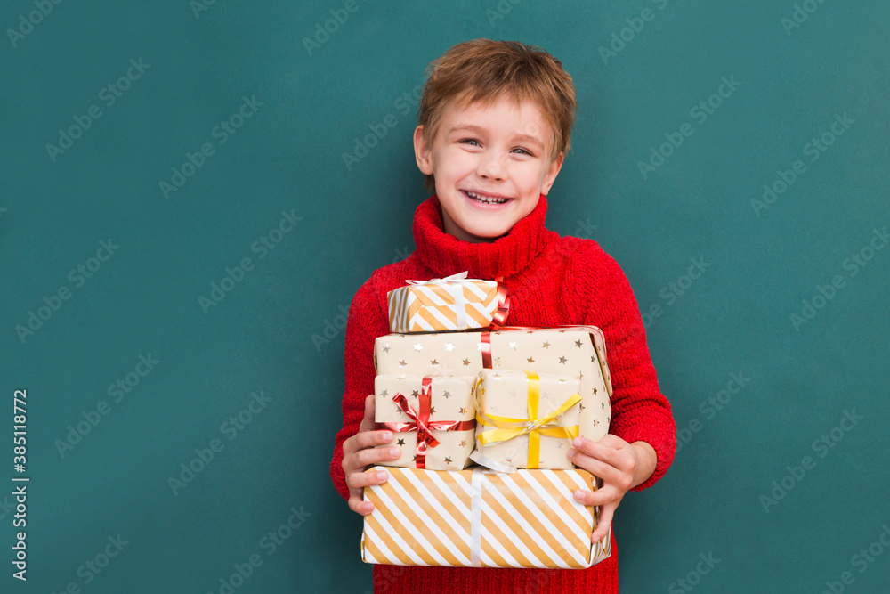 Kid boy in a red sweater with Christmas gift boxes. Christmas shopping. birthday. Copy space. new normal. Kid boy in a red sweater with Christmas gift boxes. Christmas shopping. birthday. Copy space. new normal.